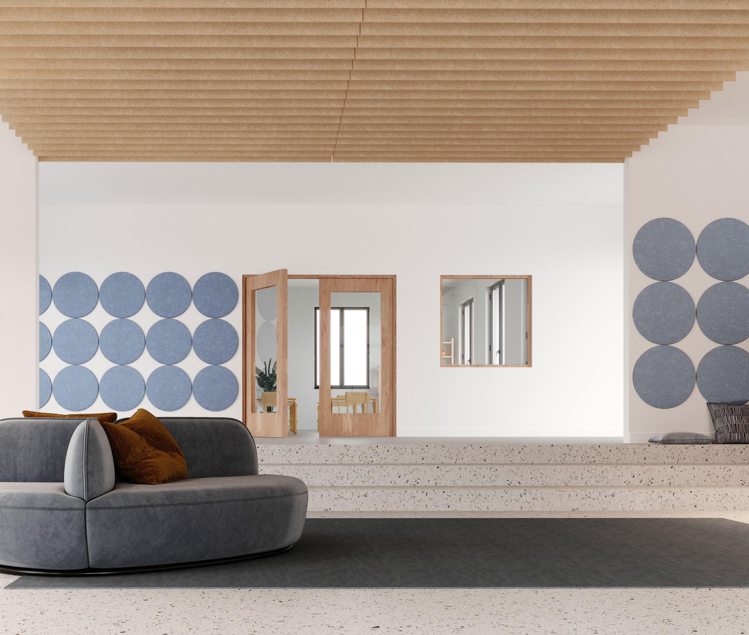 A modern interior featuring a minimalist design. A grey, semi-circular couch with burnt orange cushions is placed on polished terrazzo flooring. The white walls are adorned with circular blue acoustic felt wall tiles, and large glass doors open into another room.