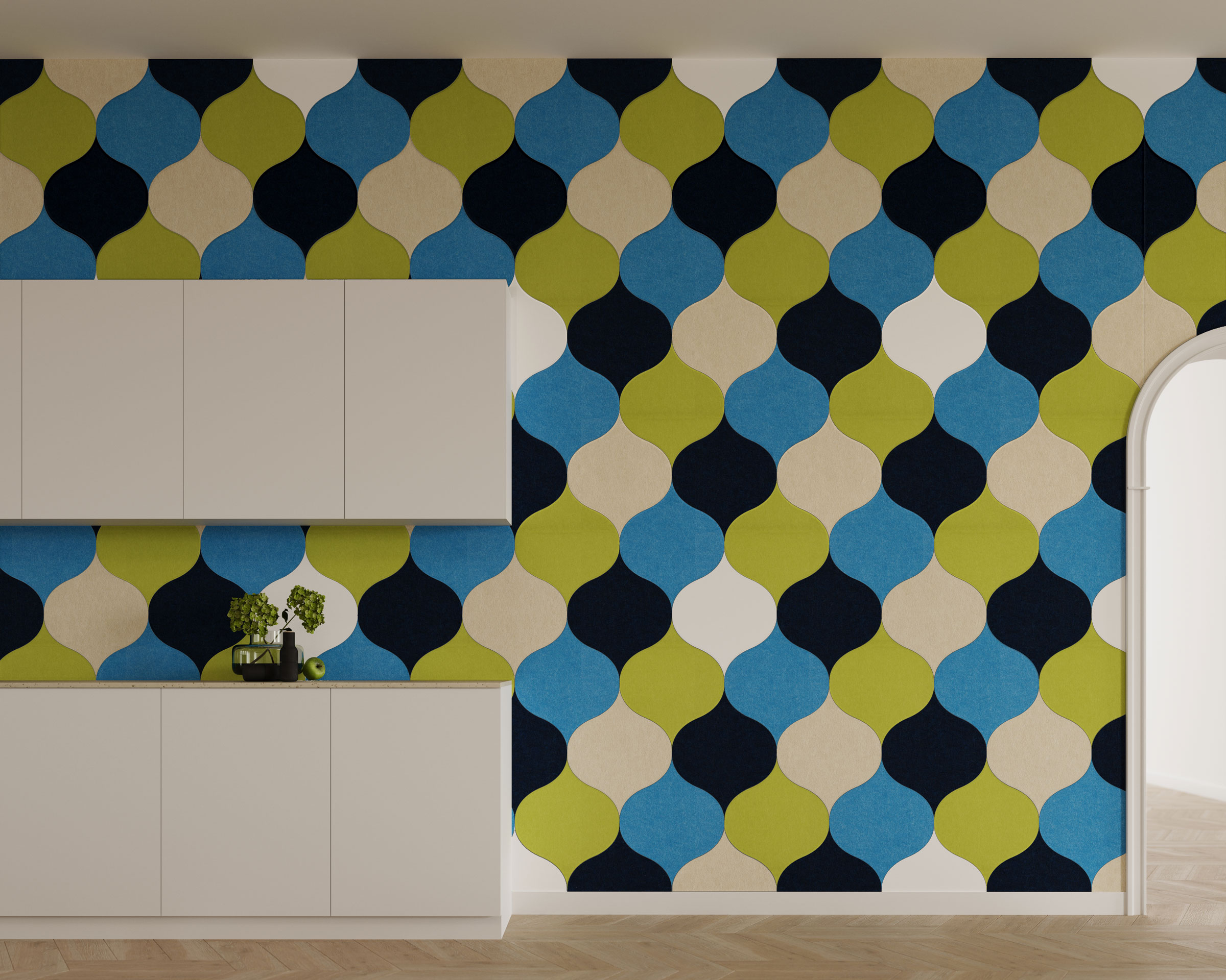 A room with a modern, geometric-patterned acoustic felt wall tiles in blue, green, black, and beige features white minimalist cabinets against the patterned wall. A small plant and decorative items are placed on the cabinets. An archway on the right leads to another area.