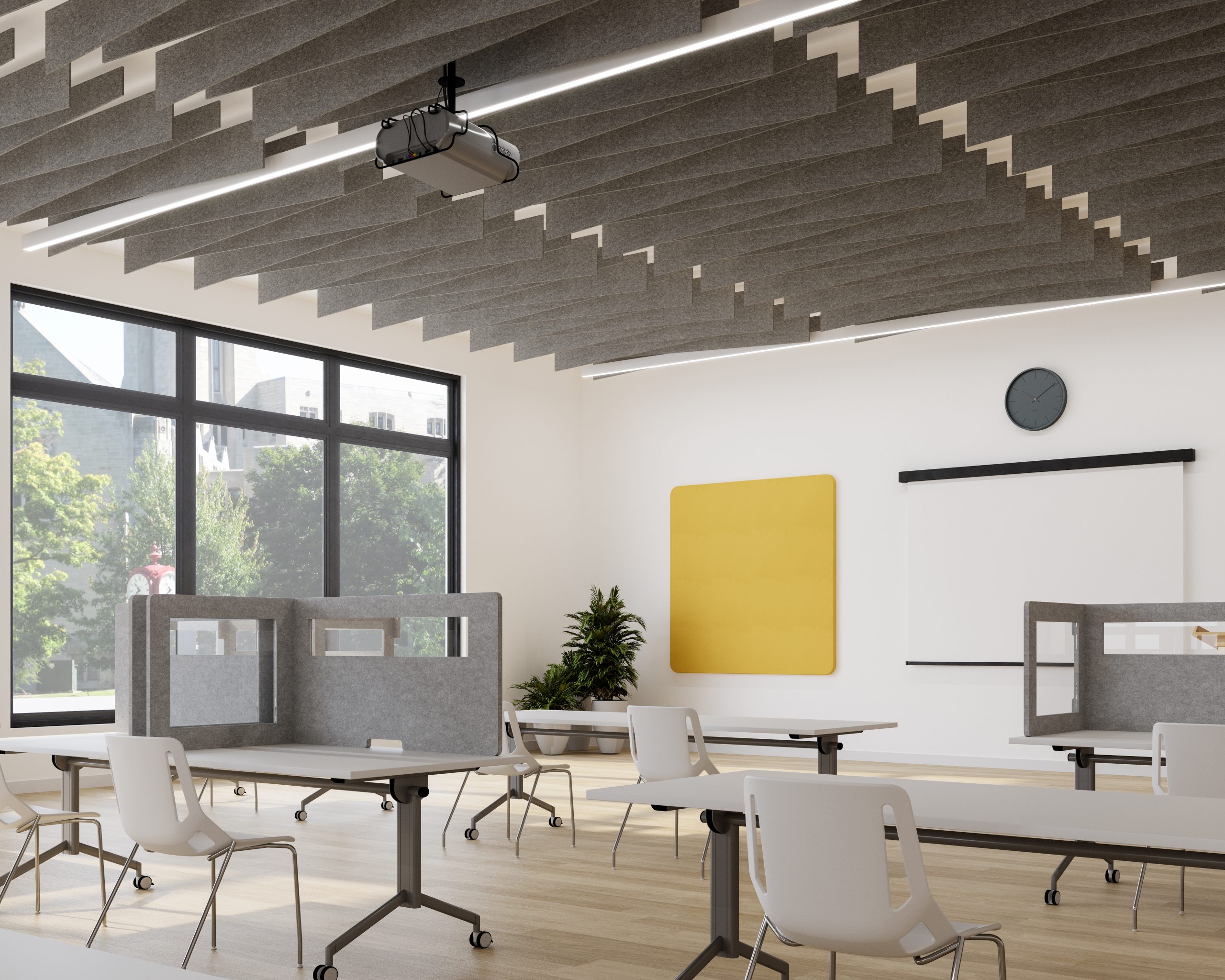 A modern classroom with individual desks and partition screens. Wing acoustic ceiling baffles hang alongside a projector from the ceiling. Large windows provide natural light, highlighting a potted plant and bright yellow wall accent. A clock and a pull-down screen are mounted on the wall.