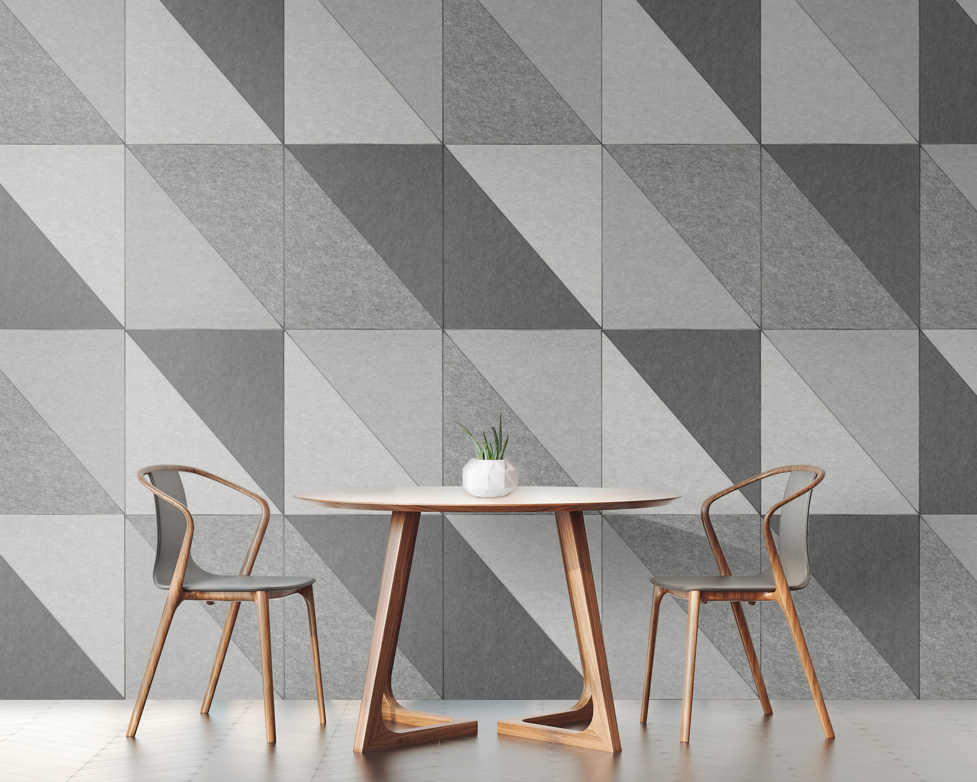 A modern interior featuring a round table with a single white vase holding a small plant. Two wooden chairs with curved backs are positioned on each side. The wall is adorned with acoustic felt wall tiles, arranged in an eye-catching geometric pattern of gray and white triangles.