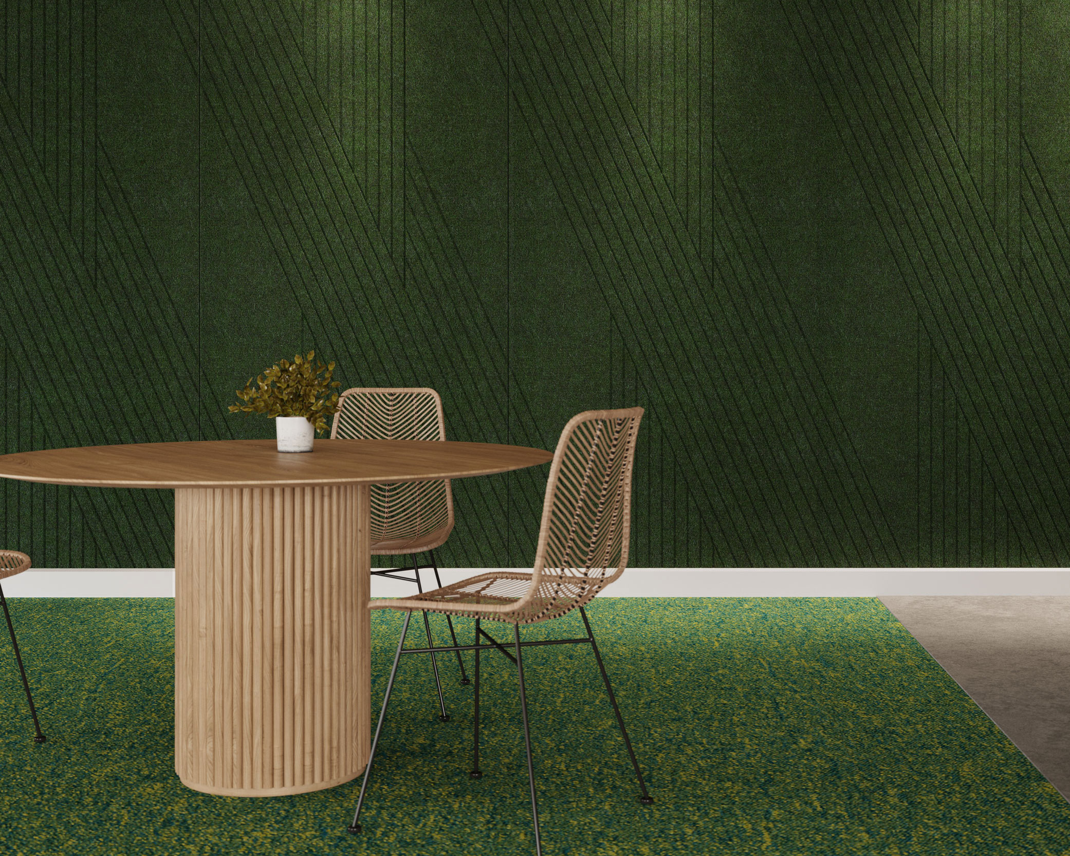 A round wooden table with a small plant in a white pot sits in front of an acoustic felt wall panel boasting green geometric patterns. Two wicker chairs with metal legs are placed on a green textured rug, and the area is illuminated by subtle overhead lighting.