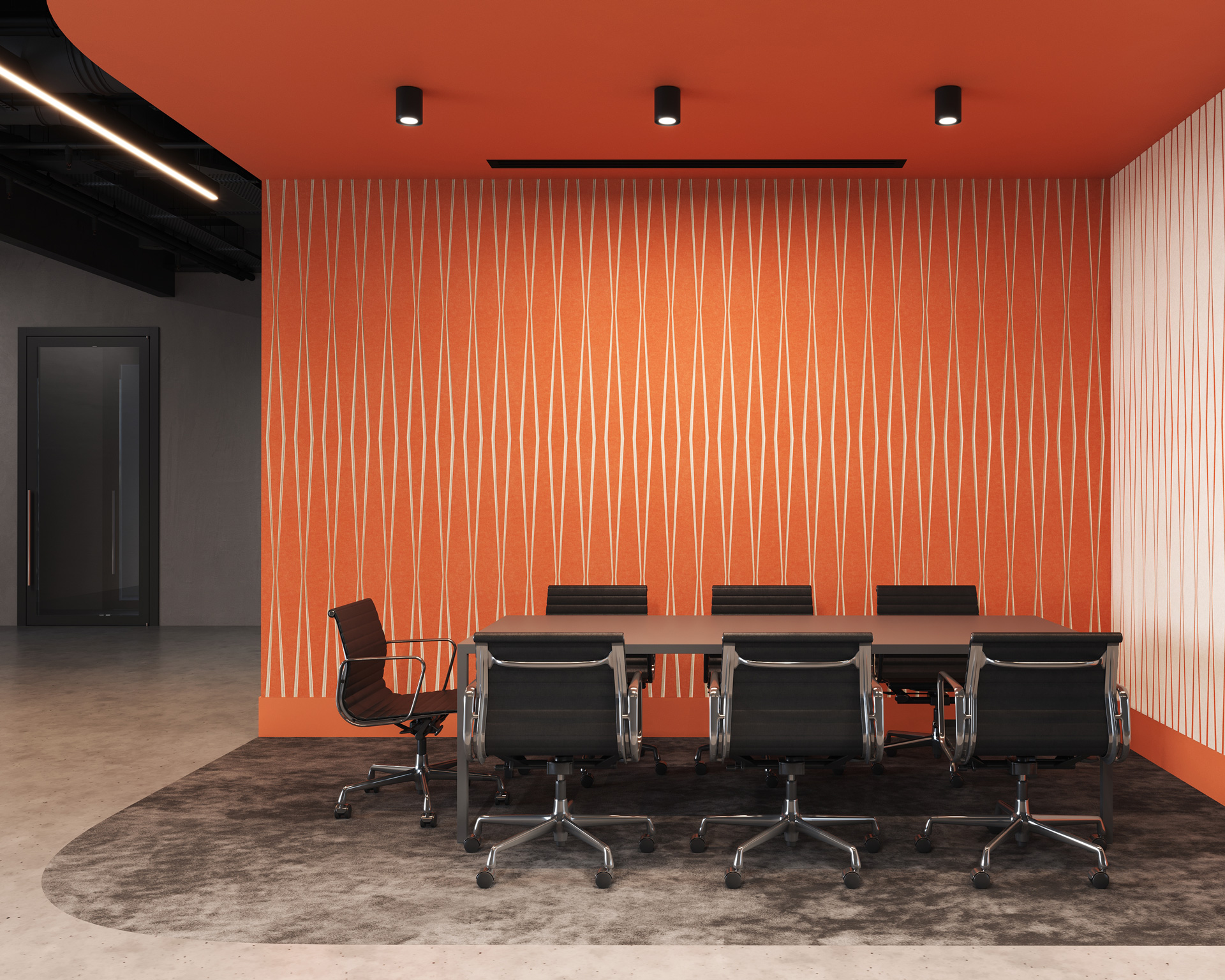 A modern conference room with an orange geometric accent wall with acoustic felt wall panels. A long rectangular table is surrounded by seven black office chairs on a gray rug. The ceiling lights are turned on, and a glass door is visible in the background.
