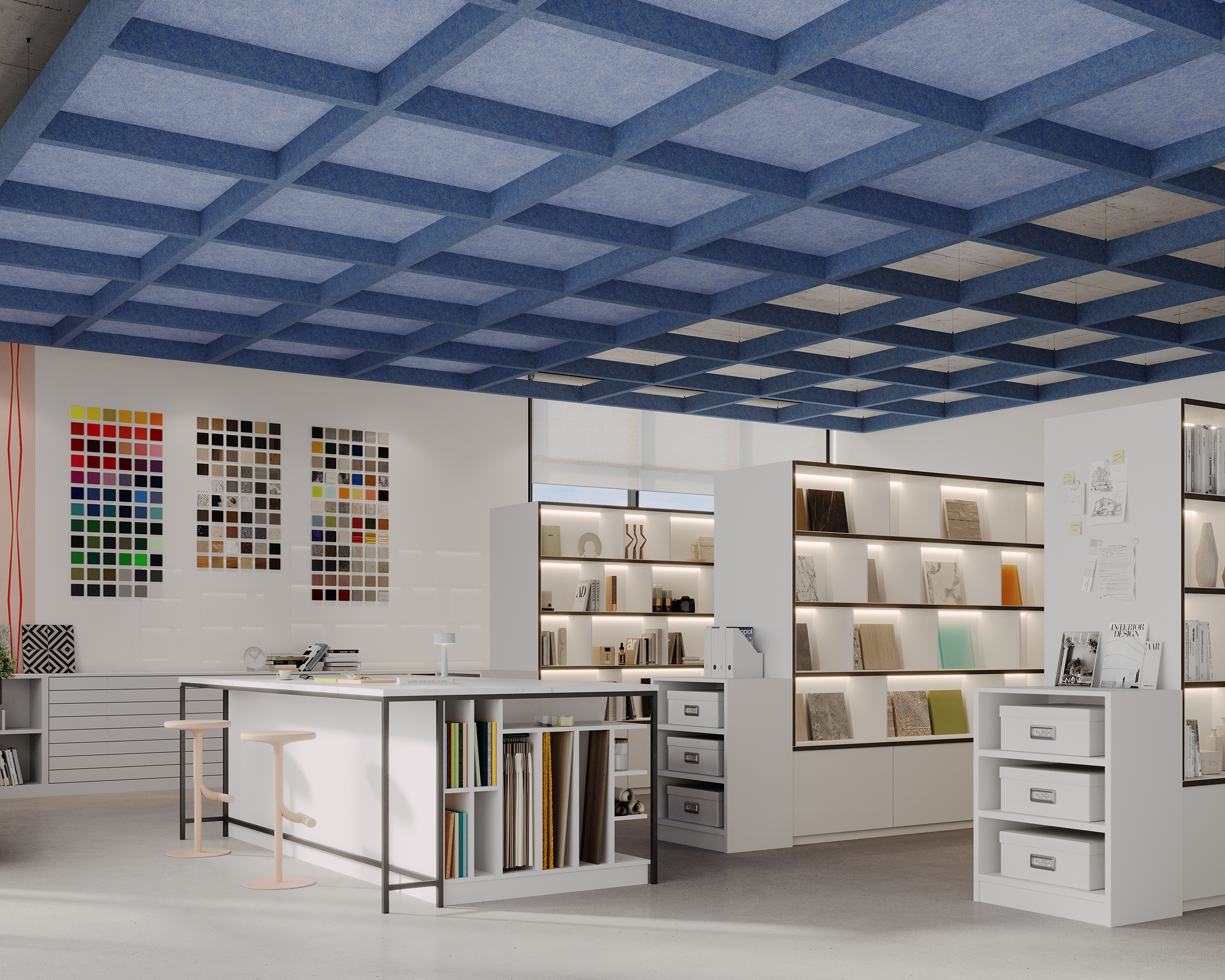 A modern interior design studio with white walls, ergonomic furniture, and a blue grid capped ceiling. The room features color swatch samples on the wall, shelving units with books and design materials, a large worktable with stools, and drawers for storage.