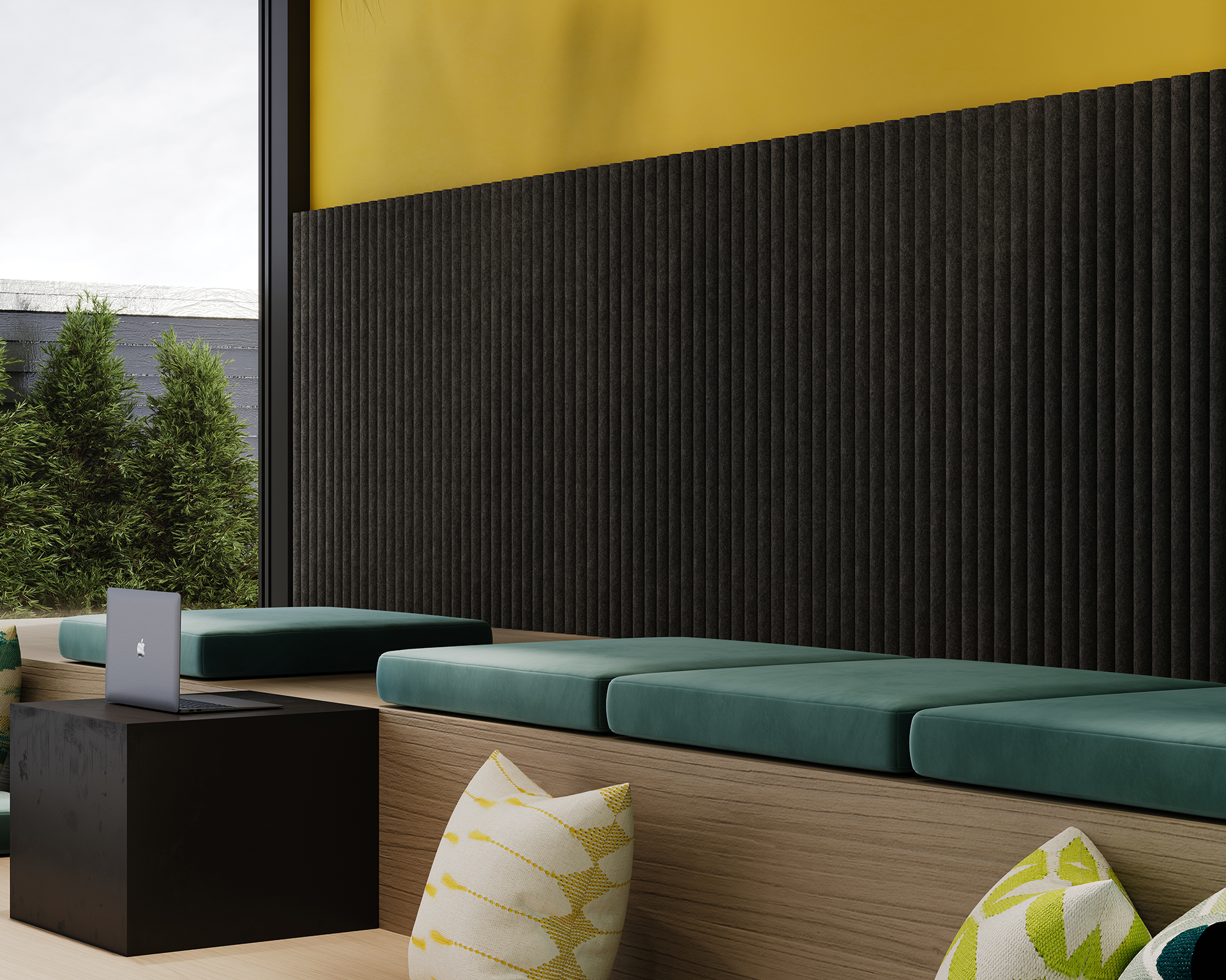 A modern seating area with wooden benches and teal cushion pads is shown. There are yellow and white patterned pillows scattered around. A black side table holds an open laptop. The wall features textured acoustic felt panels on the lower half and yellow paint on the upper half.