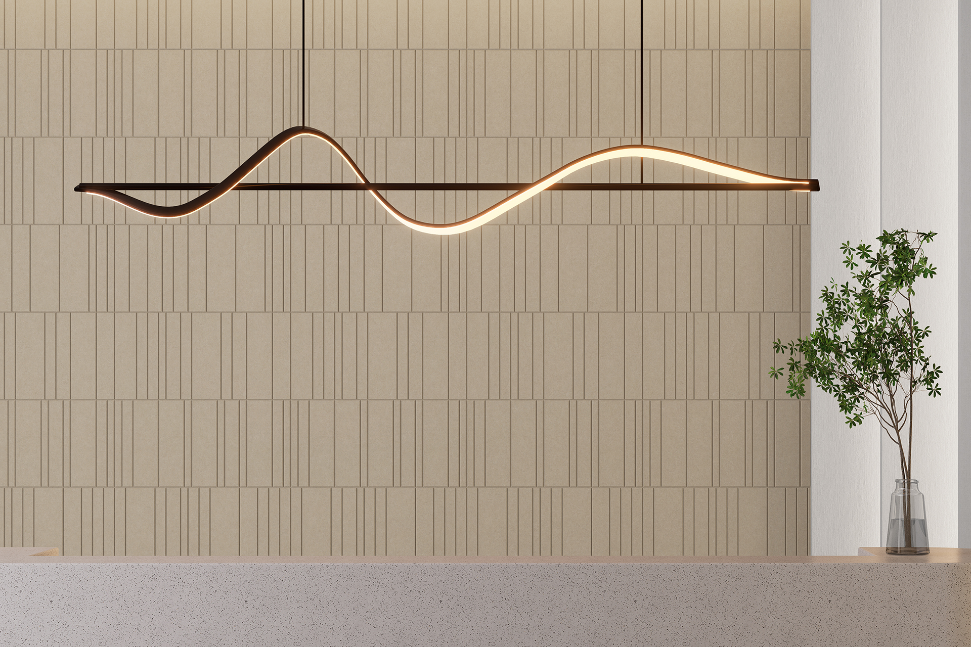 A modern, minimalist room featuring a sleek, wavy pendant light fixture hanging from the ceiling above a light-colored countertop. The backdrop has a beige textured acoustic felt wall, and a slim glass vase with a small green plant sits on the countertop.