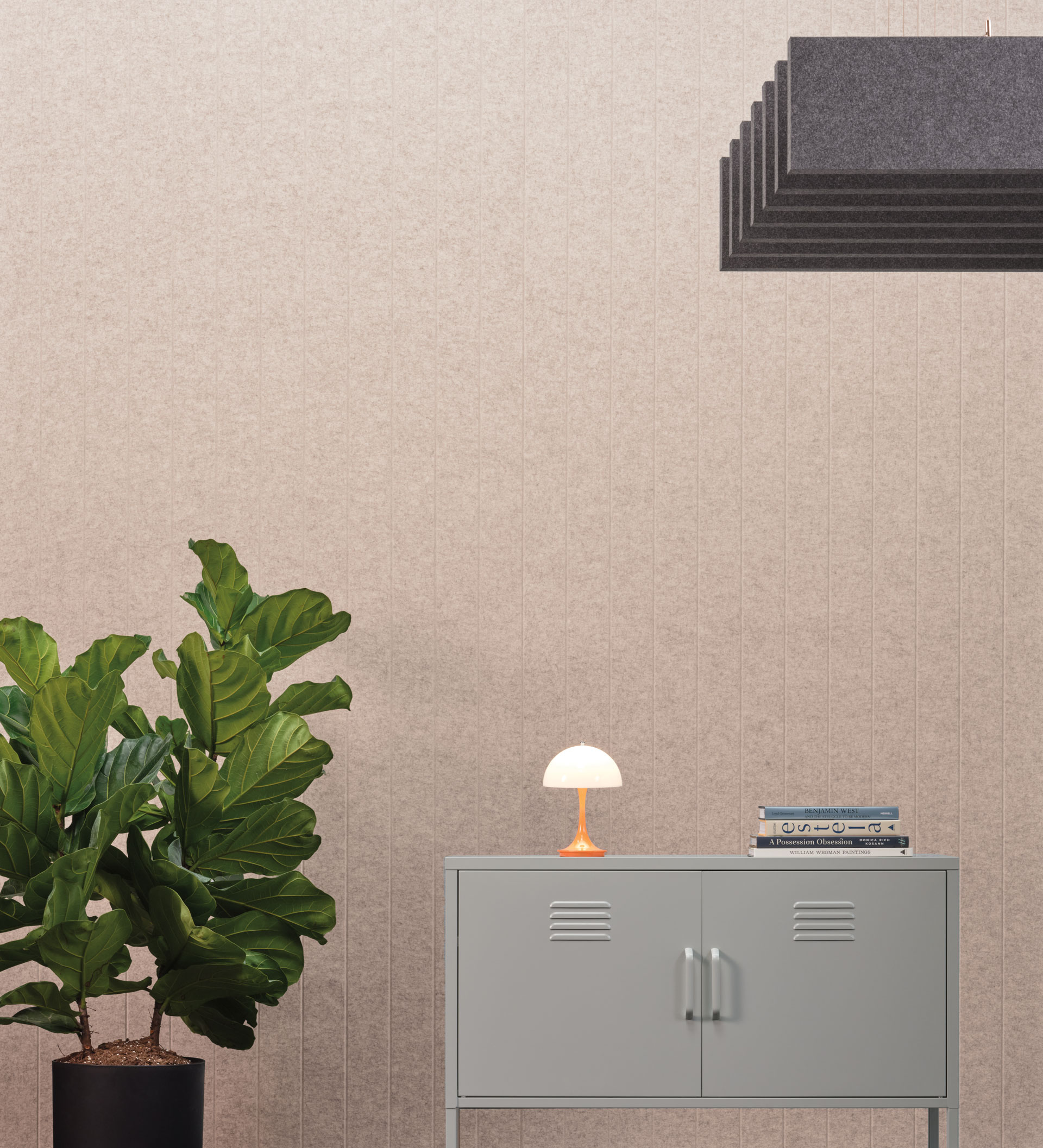 A minimalist room featuring a potted plant, a gray cabinet holding books and a small lamp, part of our premier collection, with a modern black pendant light fixture against a textured beige wall.