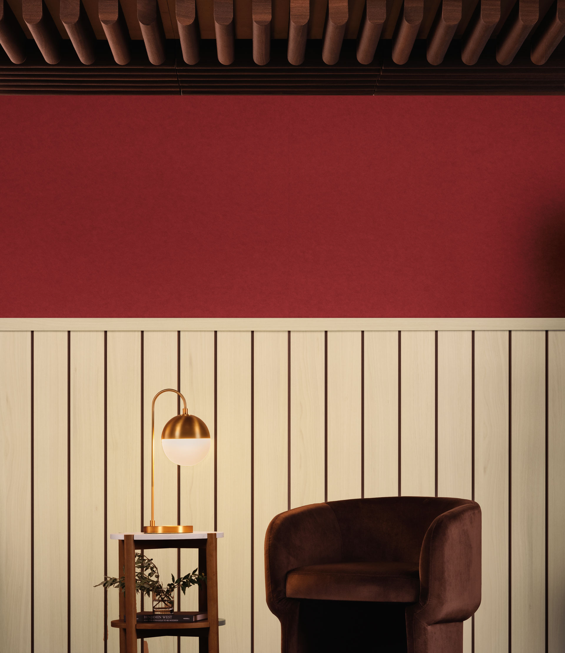 A cozy interior scene from our premier collection features a brown armchair next to a small wooden side table with a plant and a golden lamp. The wall behind the chair is divided into two sections: a wooden panel lower half and a red-painted upper half, with a wooden beamed ceiling.