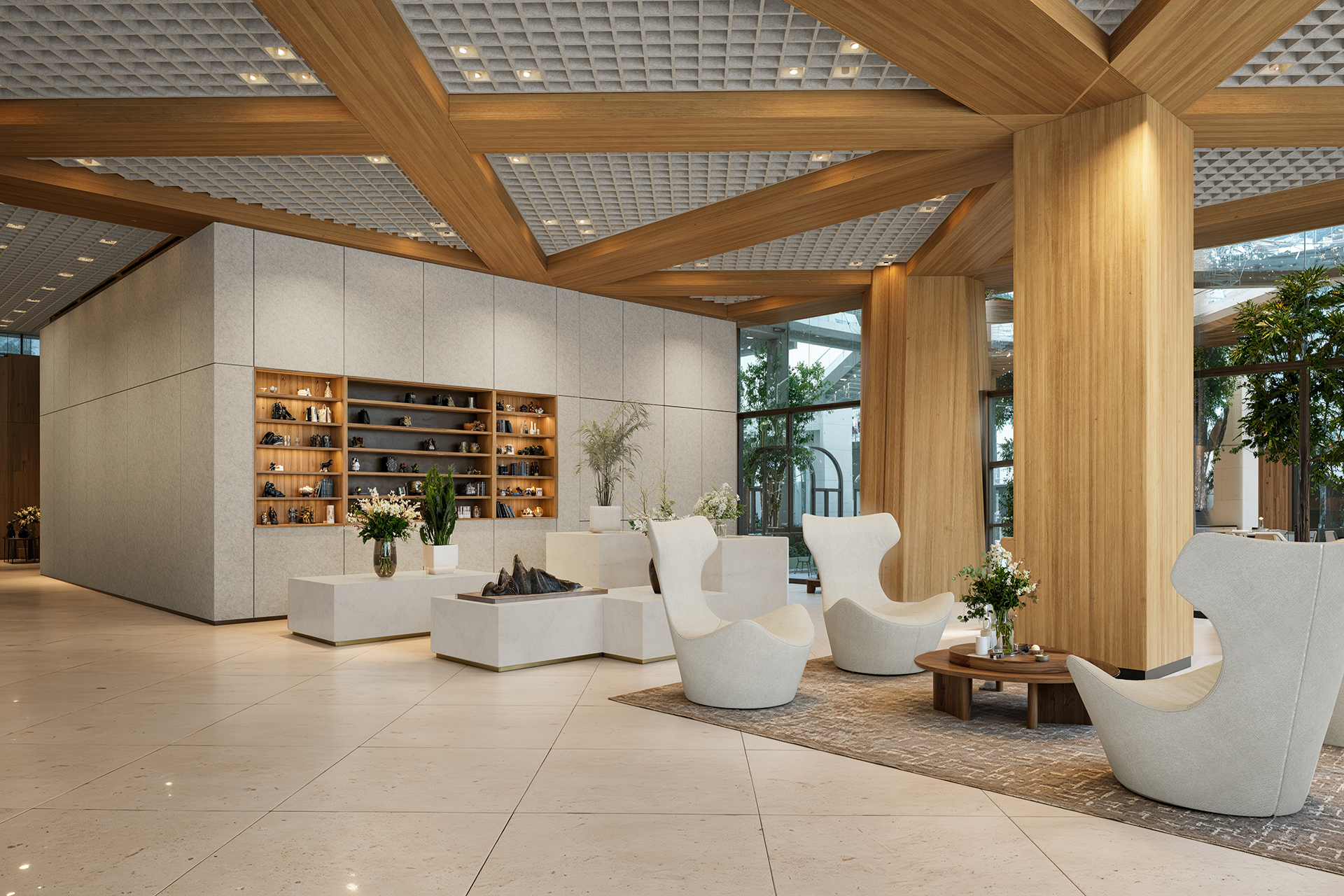 Modern interior of a lobby with wooden beams, an acoustic felt ceiling, and light tile flooring. Features white seating, a coffee table, plants, and a decorative wall with shelves. Large windows and indoor trees add a touch of nature.