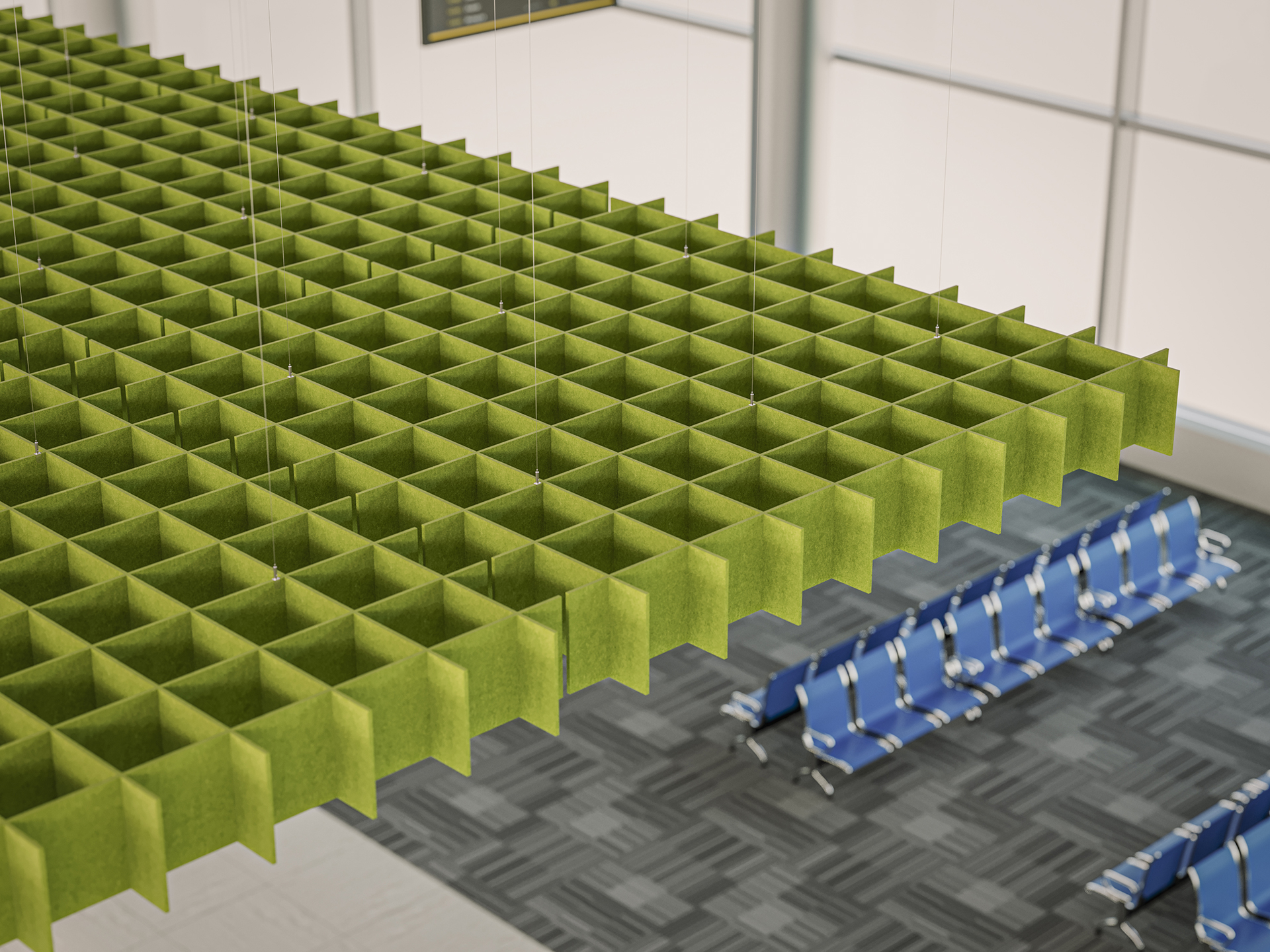 A suspended green acoustic felt panel with a grid pattern hangs from the ceiling above rows of blue chairs in a modern waiting area with large windows and carpeted flooring.